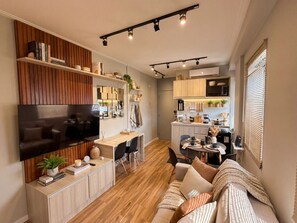 A modern living room with a flat-screen TV, wooden flooring, a sofa, a dining area, and a kitchen with wooden cabinets. - Moderno Est dio Frei Caneca a 1 km da Av Paulista (São Paulo)