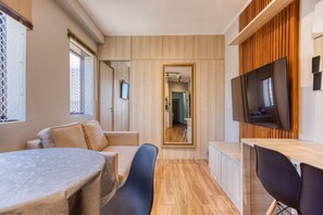 Quarto compacto e moderno com mesa de jantar, cadeiras, televisão e parede revestida de madeira.