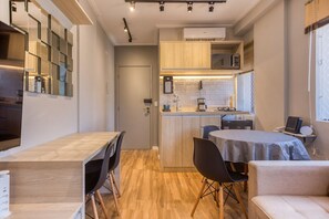 Cozinha compacta com ilha central, área de jantar com mesa e cadeiras, e um pequeno espaço de estar com sofá.