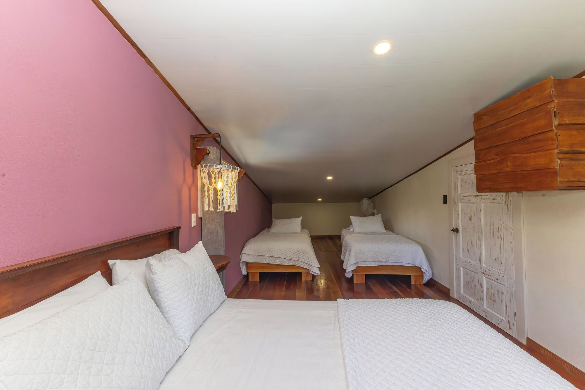 A bedroom with two beds, wooden headboards, a ceiling fan, and a wall-mounted light fixture.