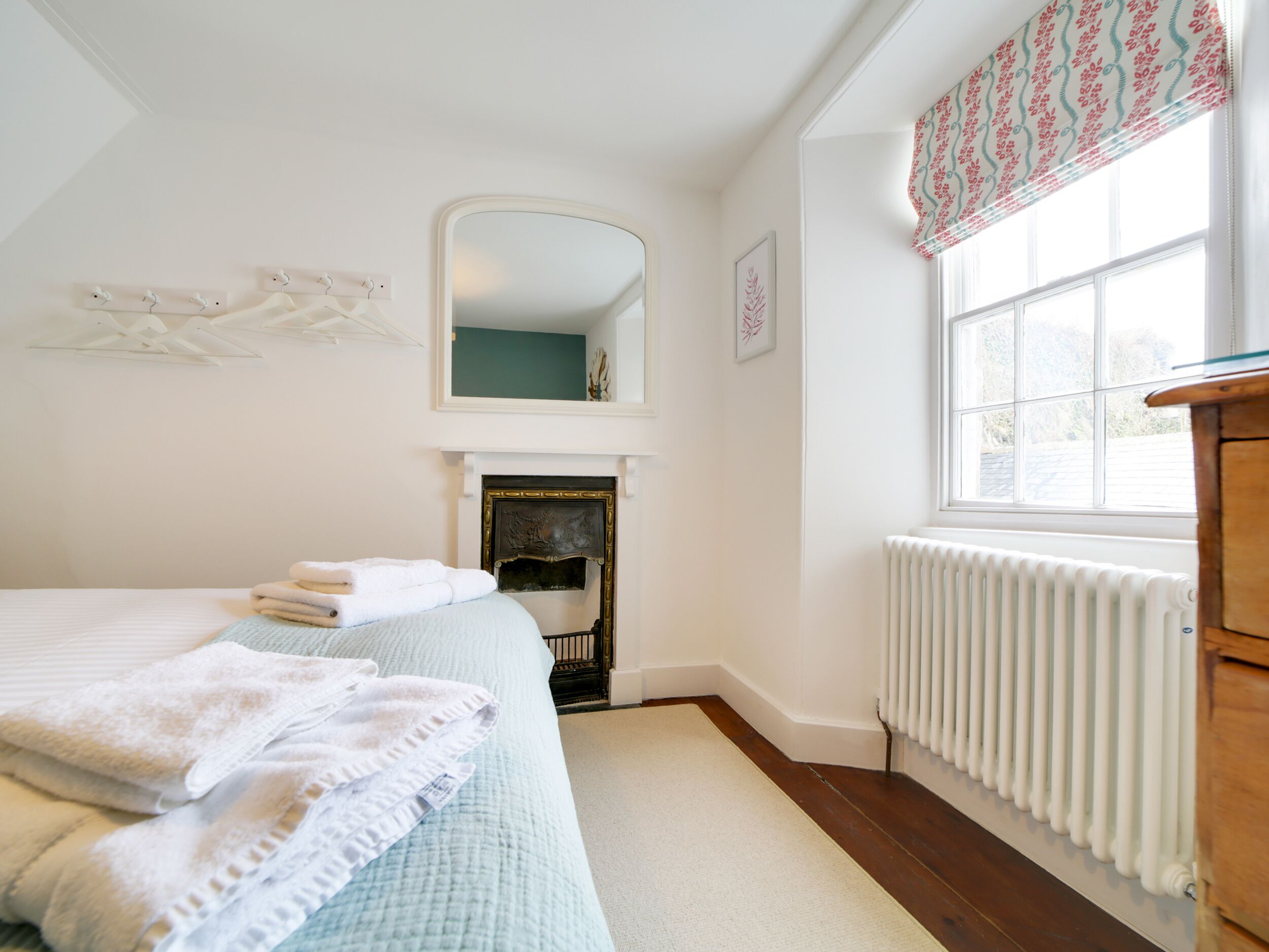 Une chambre à coucher avec un lit, une cheminée, un miroir, une fenêtre avec des rideaux et un radiateur.