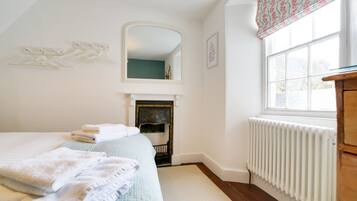 Une chambre à coucher avec un lit, une cheminée, un miroir, une fenêtre avec des rideaux et un radiateur.