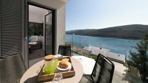 Un balcone con un tavolo apparecchiato per la colazione, vista su una baia con barche e colline.