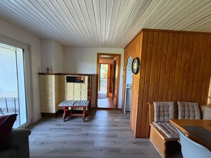 A room with a wooden bench, a small table, and a view through an open door.
