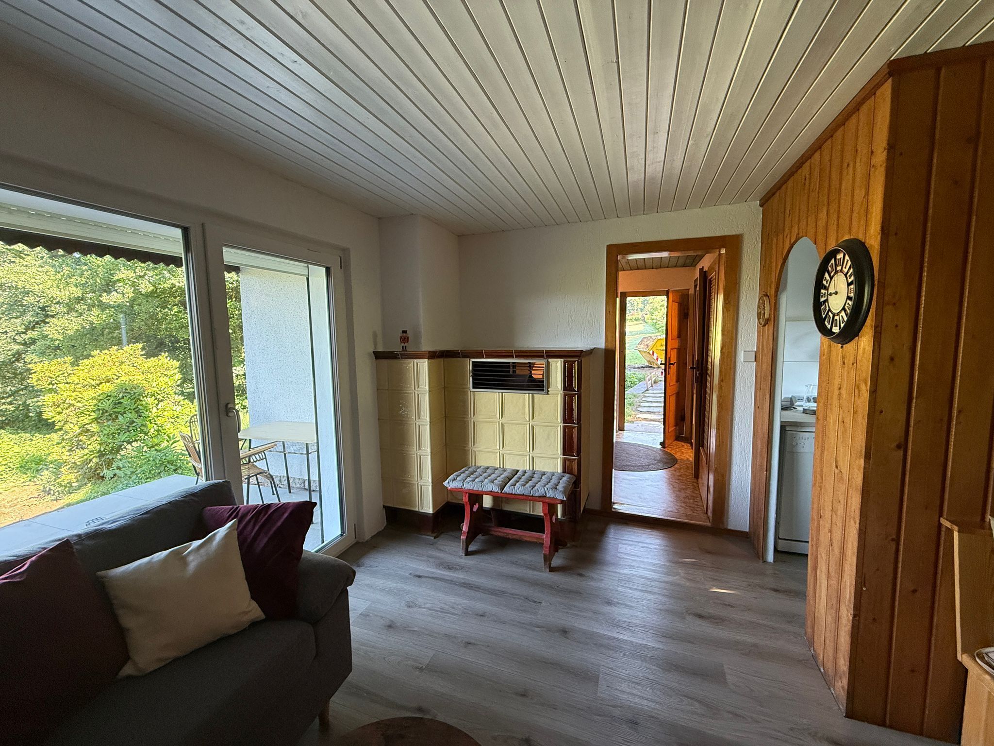 Une pièce avec un banc en bois, un canapé, une porte en bois et une vue sur la verdure à l’extérieur.