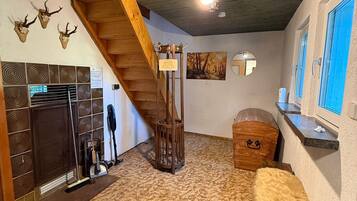 Une pièce avec un escalier en bois, une cheminée, un tapis et une malle en bois.