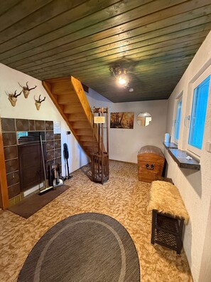A room with a wooden staircase, a fireplace, a rug, and a wooden chest.