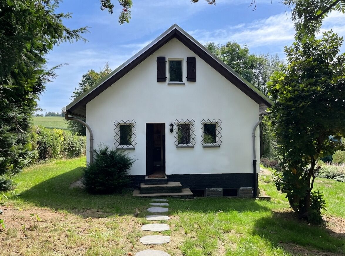 Une maison blanche d’un seul étage, avec un toit foncé, une porte d’entrée et un petit porche.
