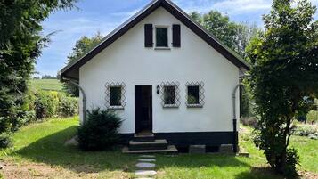 Une maison blanche d’un seul étage, avec un toit foncé, une porte d’entrée et un petit porche.