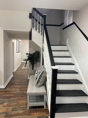 Eine Treppe mit schwarzen Geländern und weißen Stufen, die zu einer oberen Etage führt. Eine Bank mit gemustertem Kissen befindet sich am Fuß der Treppe.