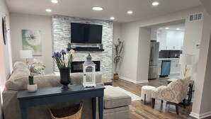 Un salon moderne avec un mur d’accent en pierre, un téléviseur à écran plat, une cheminée et un coin repas avec une cuisine en arrière-plan.