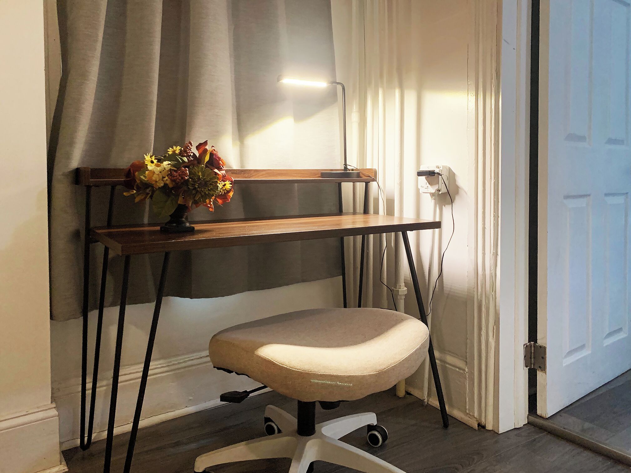 A desk with a chair, a power outlet, and a door in the background.