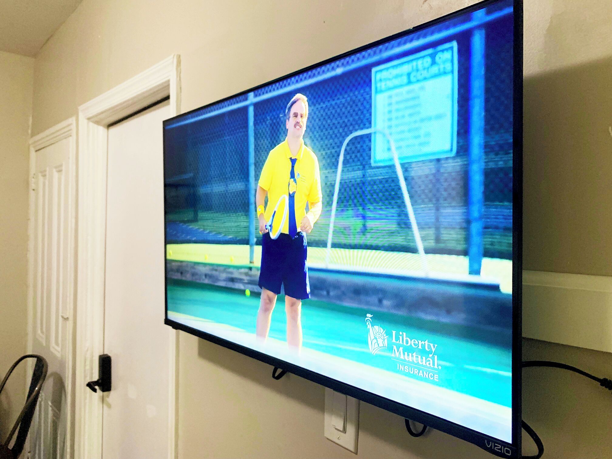 A television mounted on a wall displaying a tennis player in a yellow shirt and blue shorts.