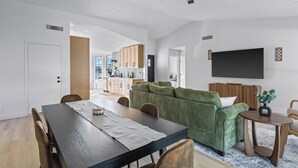A modern living room with a dining table, green sofa, and a TV mounted on the wall. - Summer Deal! Pool Home! Fast WiFi! Relocating! (Phoenix)