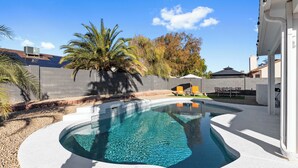A swimming pool with a curved edge, surrounded by a white deck, palm trees, and a brick wall. - Summer Deal! Pool Home! Fast WiFi! Relocating! (Phoenix)