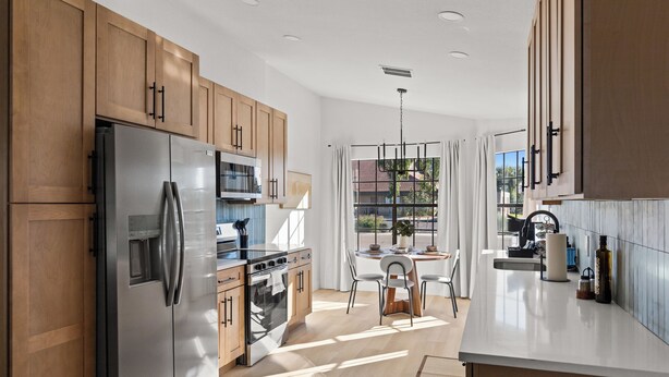 A modern kitchen with wooden cabinets, stainless steel appliances, and a dining area with a table and chairs. - Summer Deal! Pool Home! Fast WiFi! Relocating! (Phoenix)