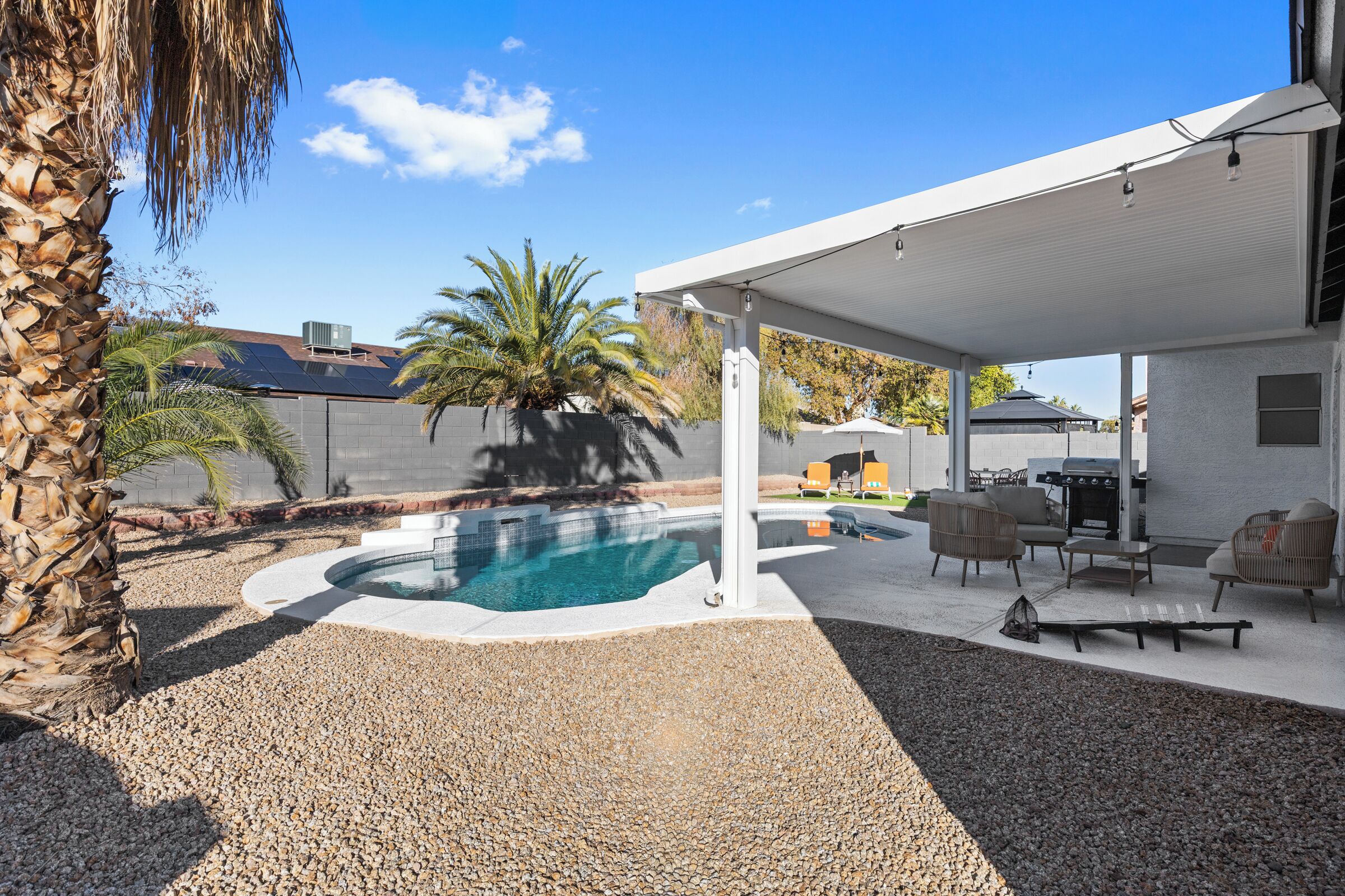 A covered outdoor area with a swimming pool, patio furniture, and a pergola.