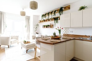 A modern kitchen with white cabinetry, wooden countertops, and a built-in island. There are shelves with plants and a variety of kitchenware. - Newport City Centre Riverside haven (Newport)