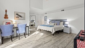 Ein modernes Schlafzimmer mit Bett, Nachttischen, einem Schreibtisch mit Stühlen, einem Deckenventilator und einer Gitarre an der Wand.