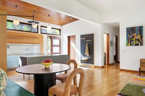 A modern kitchen with wooden cabinets, a dining area with a round table, and a staircase leading to another level. - Glass Grove (Atlanta)