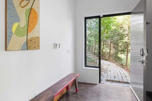 A modern room with a bench, a large abstract painting, and a sliding glass door leading to a garden. - Glass Grove (Atlanta)