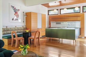 A modern kitchen with wooden cabinets, a green island, and a dining area with a round table and chairs. - Glass Grove (Atlanta)