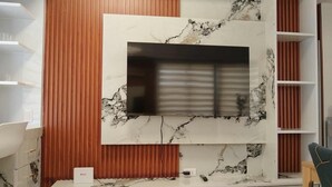 A modern living room with a marble-patterned TV wall unit, wooden paneling, and built-in shelving.