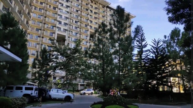 A multi-story residential building with a central courtyard, surrounded by trees and parked cars.