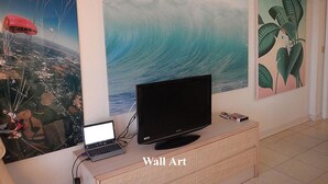 Een kamer met een televisie op een houten kast, een laptop en drie wanddecoraties met daarop een parachute, een golf en een vogel op een plant.