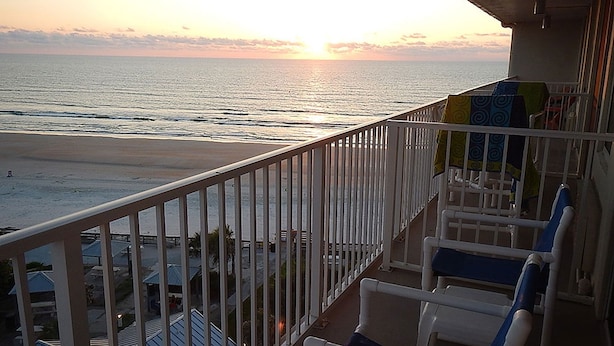 Een balkon met uitzicht op zee bij zonsondergang. Er staan stoelen en een leuning.