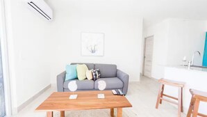 A modern living room with a grey sofa, a wooden coffee table, and a small kitchen area with a sink and stools. - Ventanas Ocean View -V3-7C- 2 bed, 2 bath (Punta Chame)