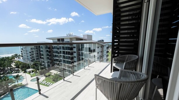 A balcony with wicker chairs, a pool, and a view of a modern building and ocean. - Ventanas Ocean View -V3-7C- 2 bed, 2 bath (Punta Chame)