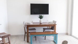 A dining area with a wooden table, two chairs, a bench, a flat-screen TV mounted on the wall, and a potted plant. - Ventanas Ocean View -V3-7C- 2 bed, 2 bath (Punta Chame)