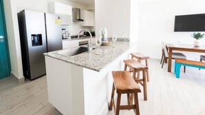A modern kitchen with a granite countertop, stainless steel appliances, and a dining area with wooden stools. - Ventanas Ocean View -V3-7C- 2 bed, 2 bath (Punta Chame)