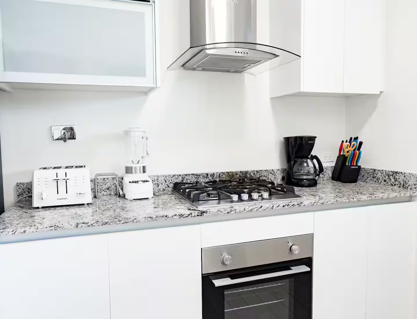 Una cocina moderna con armarios blancos, estufa integrada, cafetera y licuadora.
