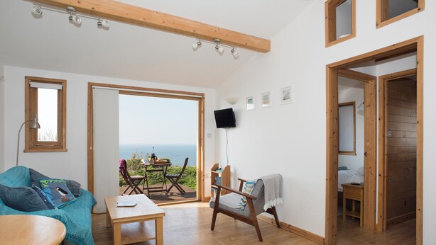 Un vaste espace de vie doté d’un plancher en bois, d’un canapé, d’une table et d’une chaise. Un balcon offre une vue sur la mer.