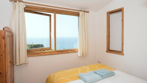 Une chambre à coucher avec un lit, une fenêtre avec des rideaux, une armoire en bois et un miroir au mur.