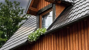 A wooden cabin with a sloped roof, a dormer window, and a small window with white flowers. - Etno house Molendini (Čatrnja)