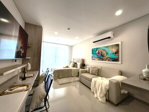A modern living room with a sofa, a dining area with a table and chairs, a painting on the wall, and a television mounted on the wall. - Apartamentos Reserva del Mar II-by SOHO (Santa Marta)