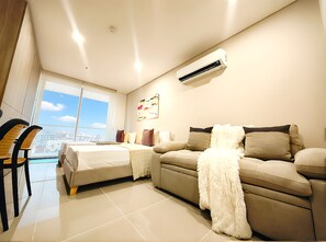 A modern hotel room with a bed, sofa, and a view of the city. - Apartamentos Reserva del Mar II-by SOHO (Santa Marta)