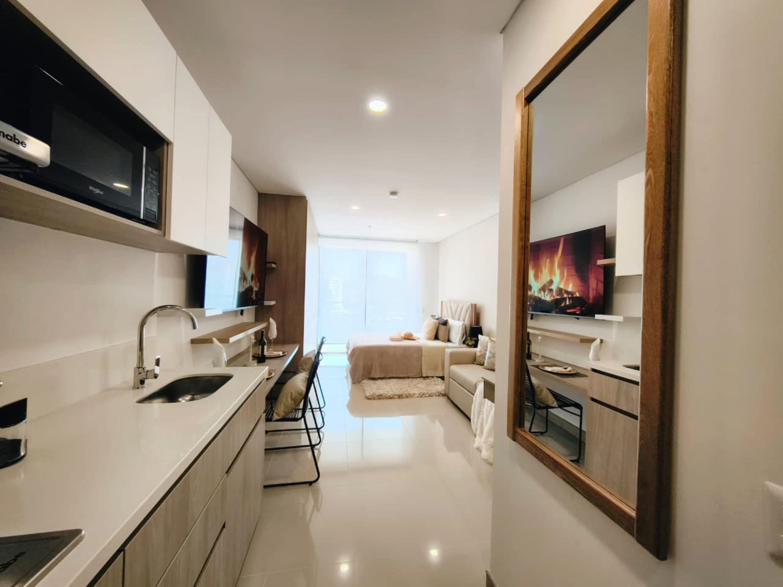 A modern kitchen with a built-in oven, a dining area with a sofa, and a large mirror.