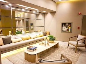 A modern living room with a sofa, coffee table, and armchair, a large mirror, and a framed picture on the wall.