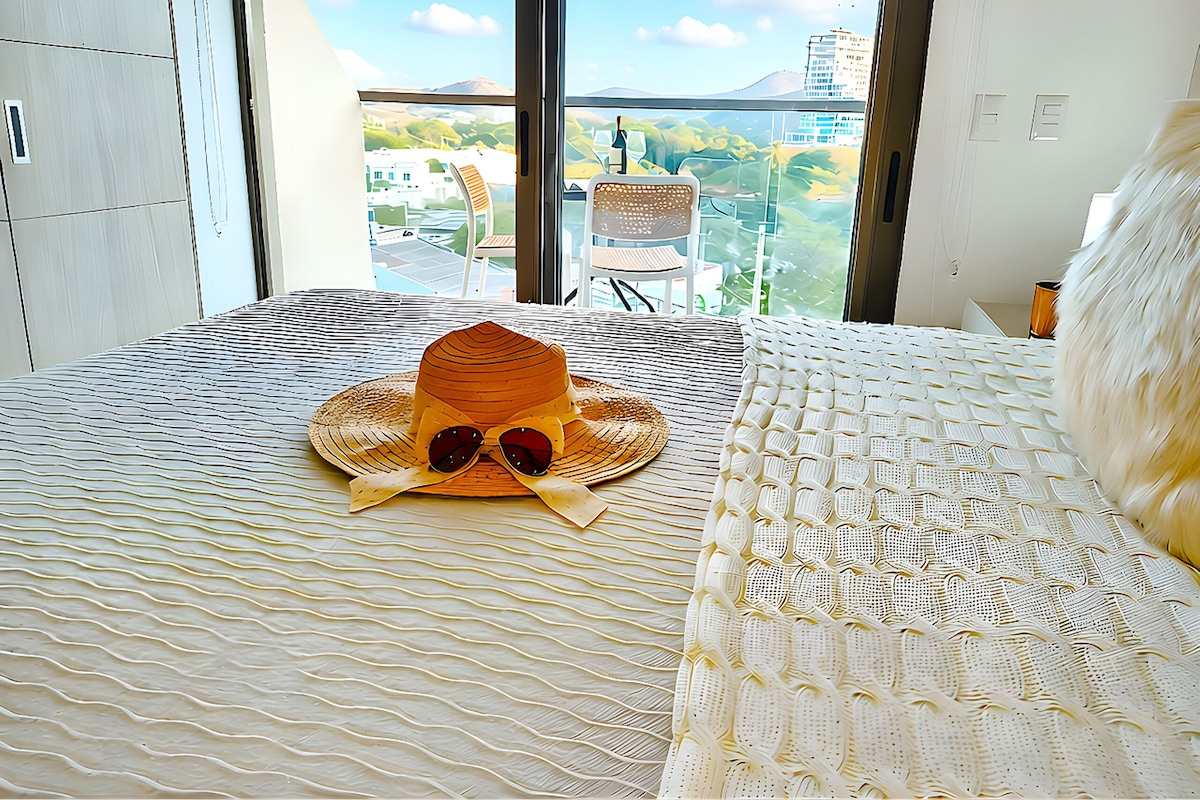 A hotel room with a bed, a window with a view of a cityscape, and a chair by the window.