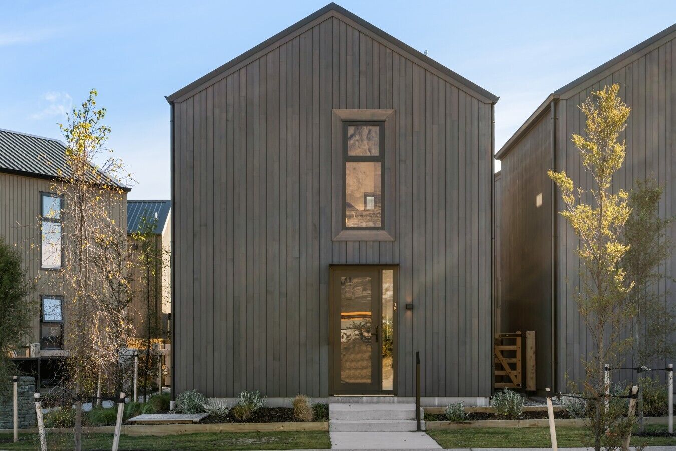 Un bâtiment moderne doté d’une façade verticale en bois, d’une entrée centrale et d’une petite fenêtre située au-dessus de la porte.