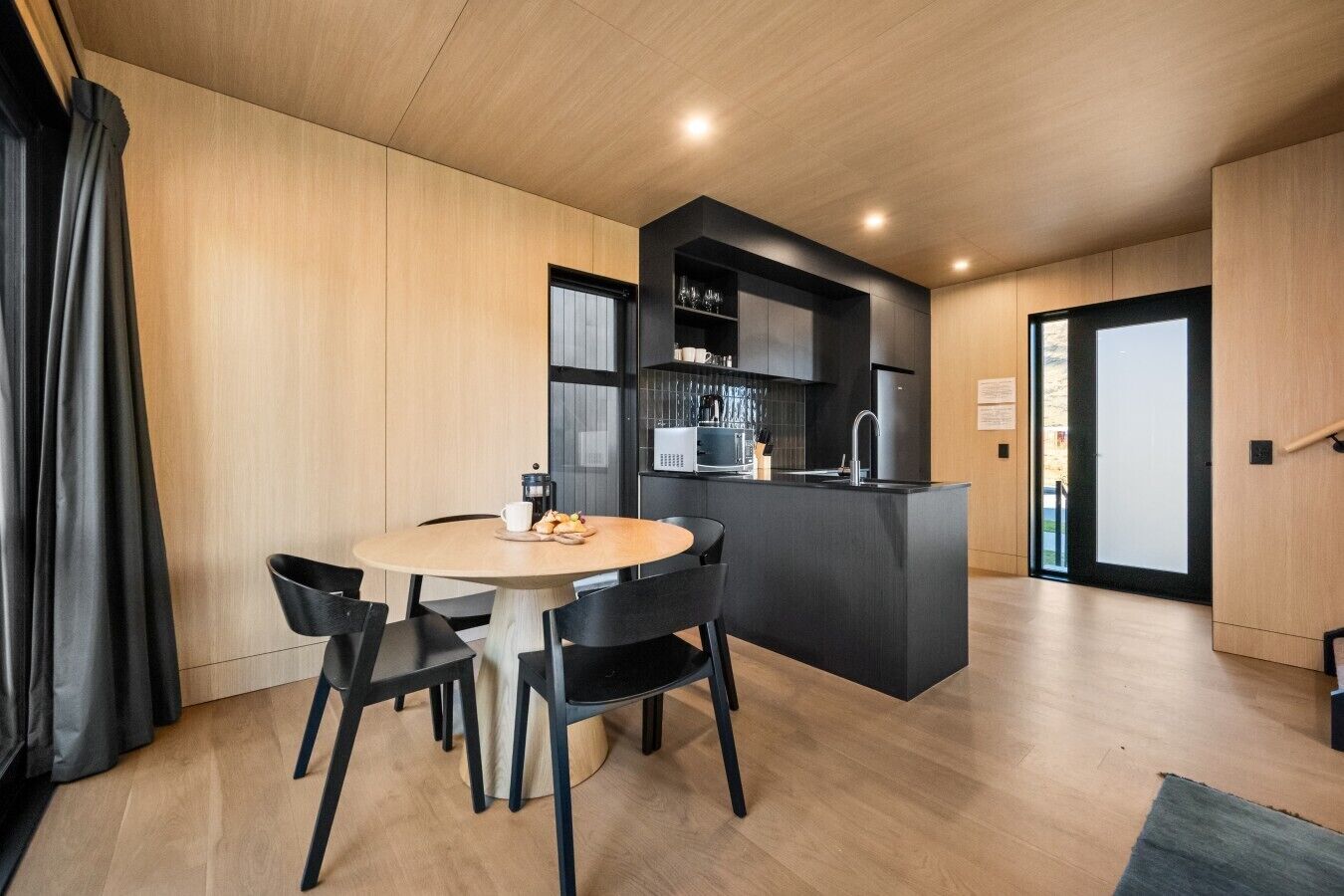 Une cuisine moderne dotée d’un îlot central, d’un coin repas avec une table ronde et des chaises, et offrant une vue à travers une porte vitrée.