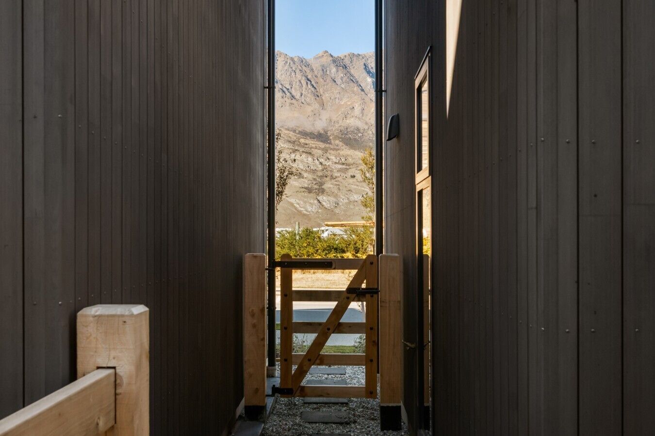 Un couloir étroit mène à une porte, avec un paysage montagneux en arrière-plan.