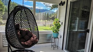 A hanging chair with a cushioned seat on a porch, a potted plant, and a view of a mountain landscape. - Private Ranch House, Highland Cattle, Horses & Peaceful Views - a soul refresher (Myrtle Creek)