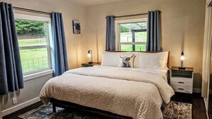 A bedroom with a large bed, two bedside tables with lamps, a window with curtains, and a view of a garden. - Private Ranch House, Highland Cattle, Horses & Peaceful Views - a soul refresher (Myrtle Creek)