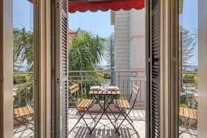 An outdoor balcony with a table set for two, a chair, and a potted plant.