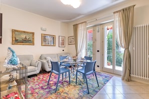 A living room with a sofa, chairs, a glass-top dining table, and a colorful rug. - Palm House apartment in elegant, central setting, a few steps from the sea. (Bordighera)